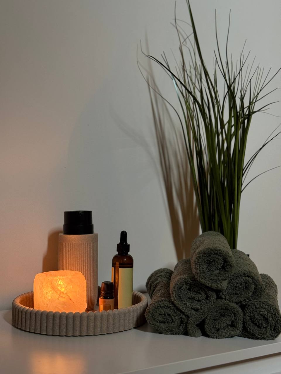Een brandende zoutlamp, flesjes olie en opgerolde groene handdoeken