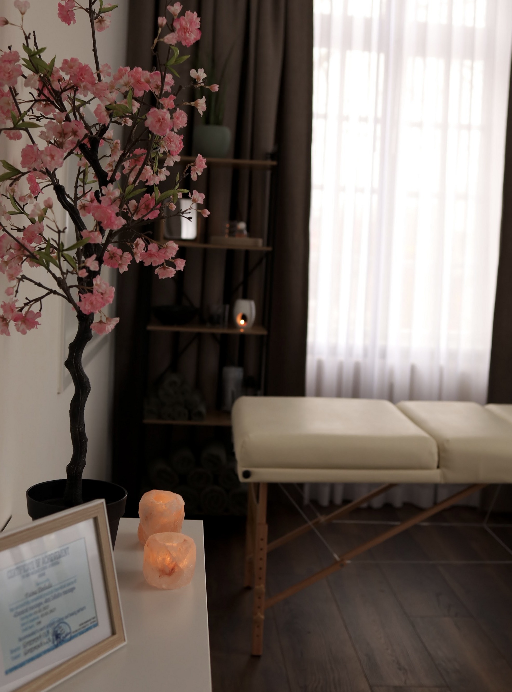 De massagetafel bij het raam, naast een boom met roze bloesem