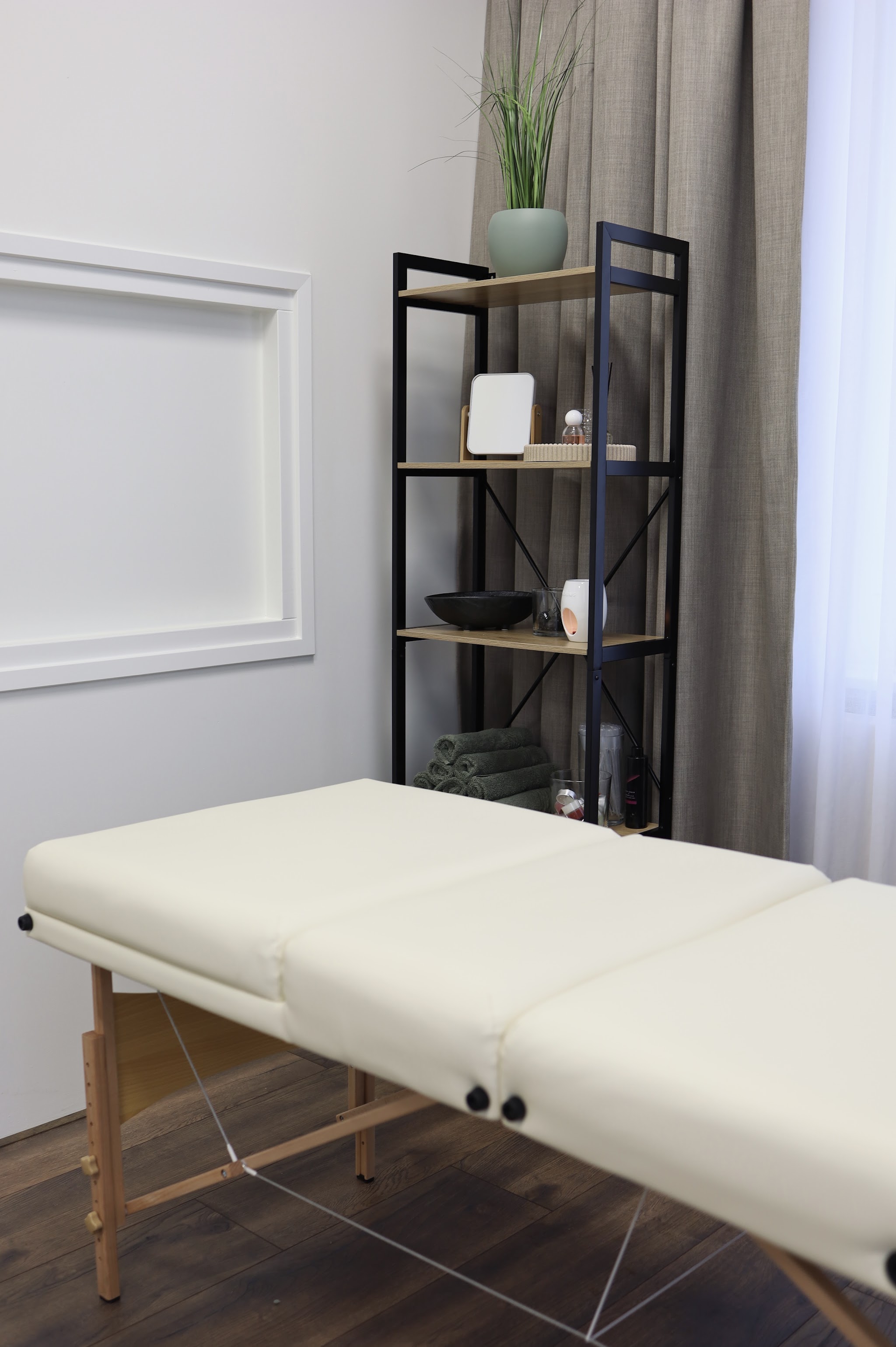 De crèmekleurige massagetafel bij het raam, met een plant en een open kast